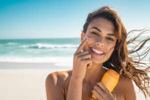 Woman on beach applying mineral sunscreen to face to avoid breakouts.