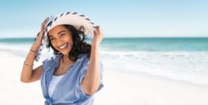Woman on beach wearing protective clothing and sunhat to prevent melanoma.
